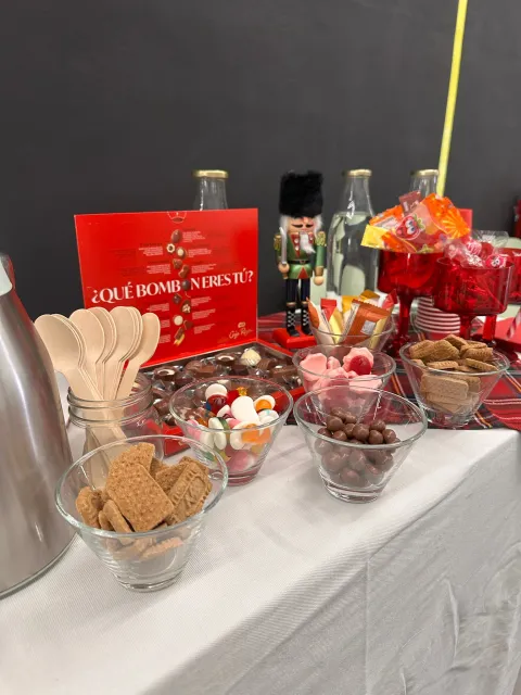 Mesa de dulces con el cartel ¿Qué bombón eres tú?, cuencos de chuches y chocolatinas