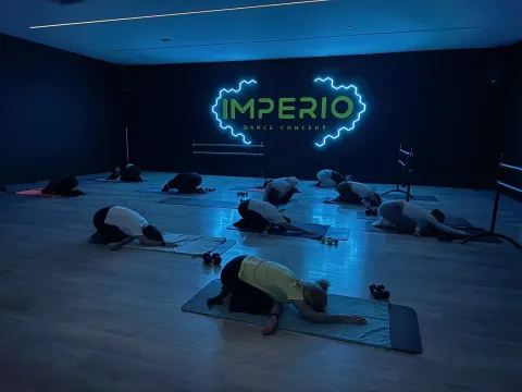 Grupo en postura del niño sobre esterillas en sala Imperio Dance Concept con luz azul