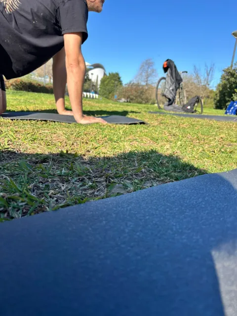Participante en postura cuadrúpeda sobre esterilla en parque, plano a ras de suelo