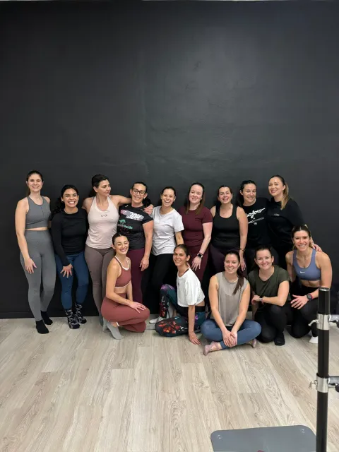 Foto grupal de participantes del taller en sala de fitness contra pared oscura