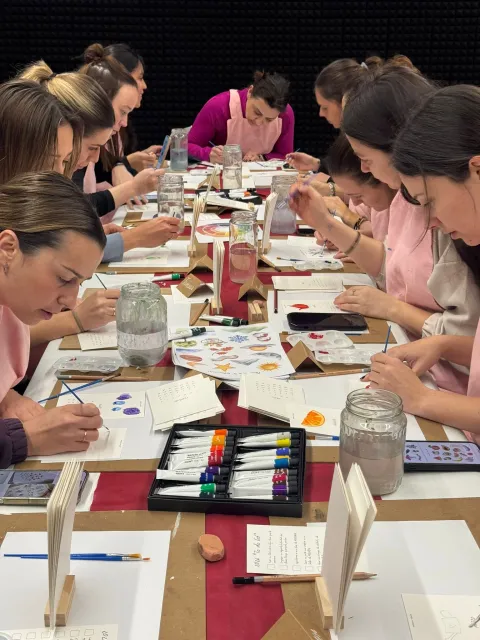 Participantes pintando con acuarela en taller creativo sentadas en larga mesa