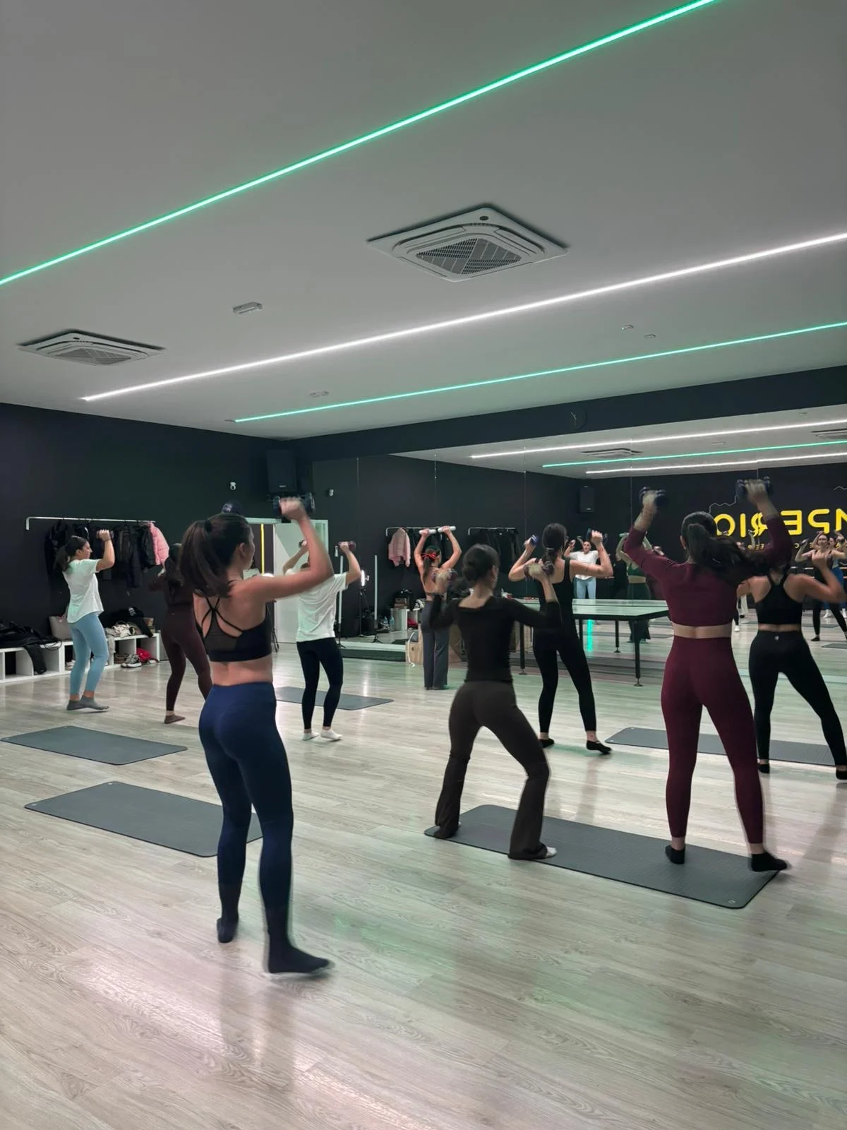Clase grupal de fitness con mancuernas en estudio con iluminación neón verde